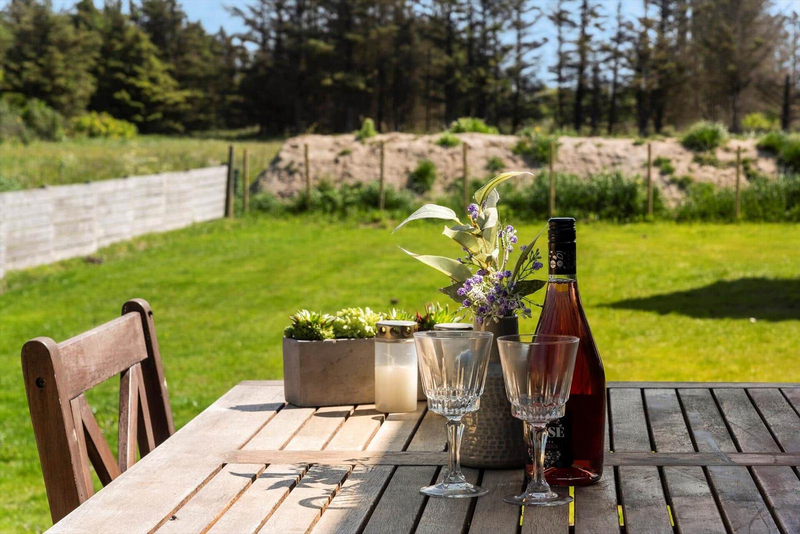 Holztisch mit Wein, Gläsern und Pflanzen im Garten.