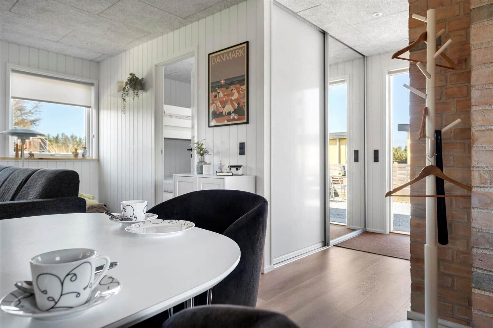 Essbereich mit Tisch, Stühlen und Blick auf Balkon. Wandbild und Kleiderständer sichtbar.