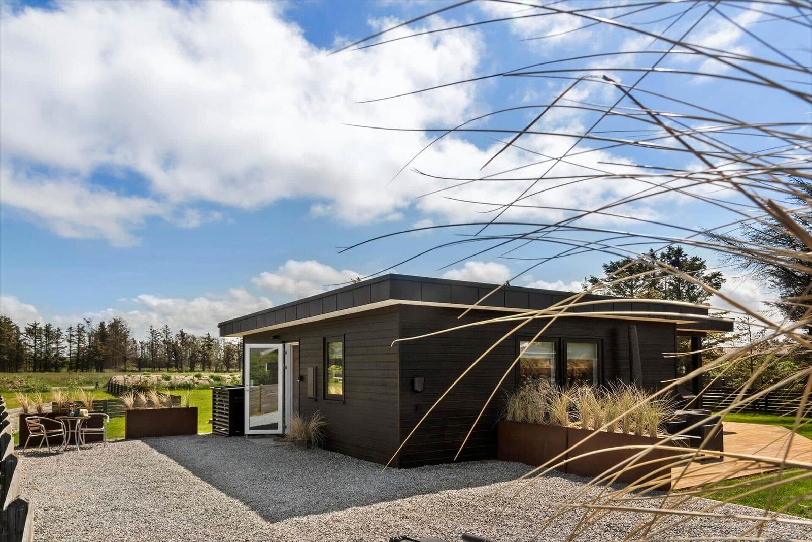 Moderne Holzhütte mit Terrasse und Garten unter blauem Himmel.