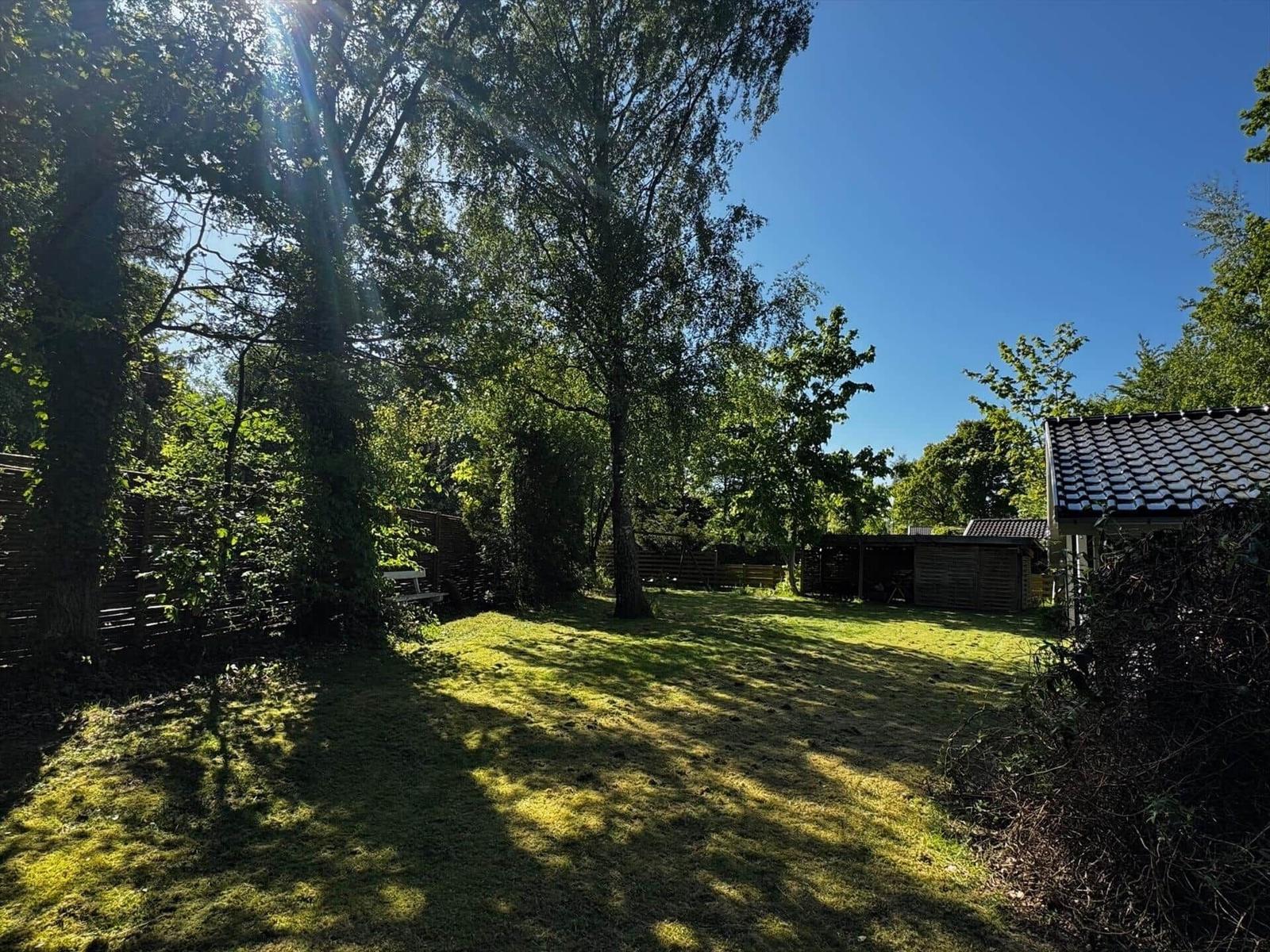 Green garden with trees and small wooden house under blue sky.