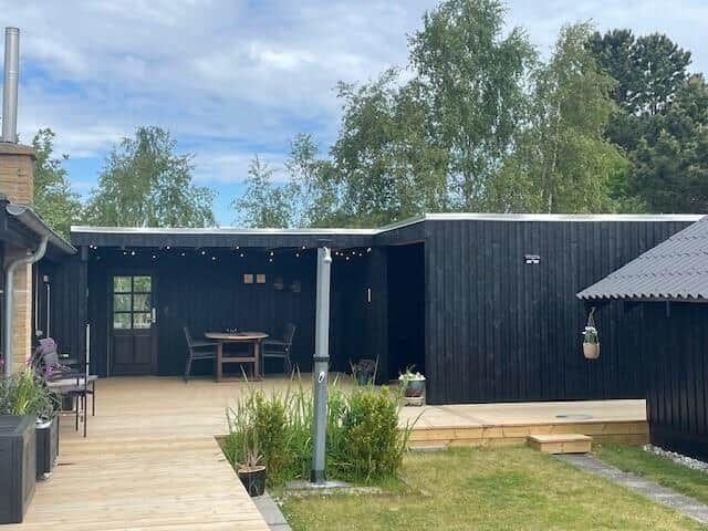 Schwarzer Holzausbau mit Terrasse, Tisch, Stühlen und Pflanzen im Garten.