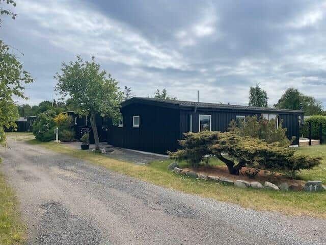 Schwarzes Holzhaus mit Garten und Kiesweg unter bewölktem Himmel.