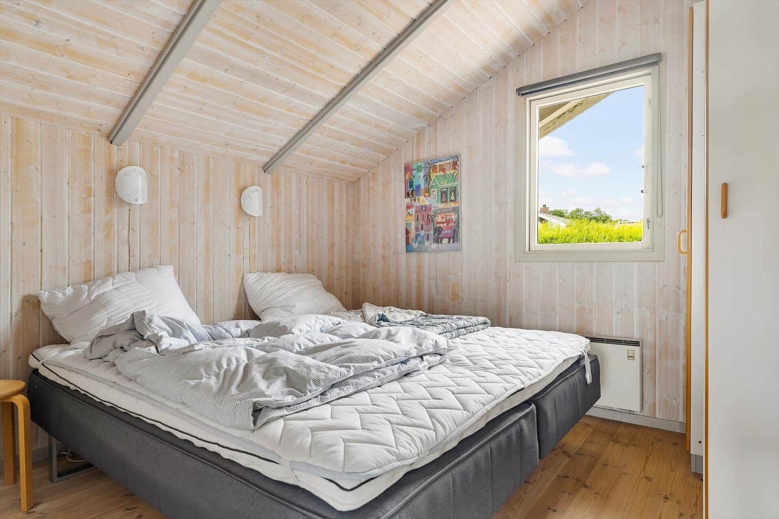 Bedroom with wooden walls, bed, and window with view of green.