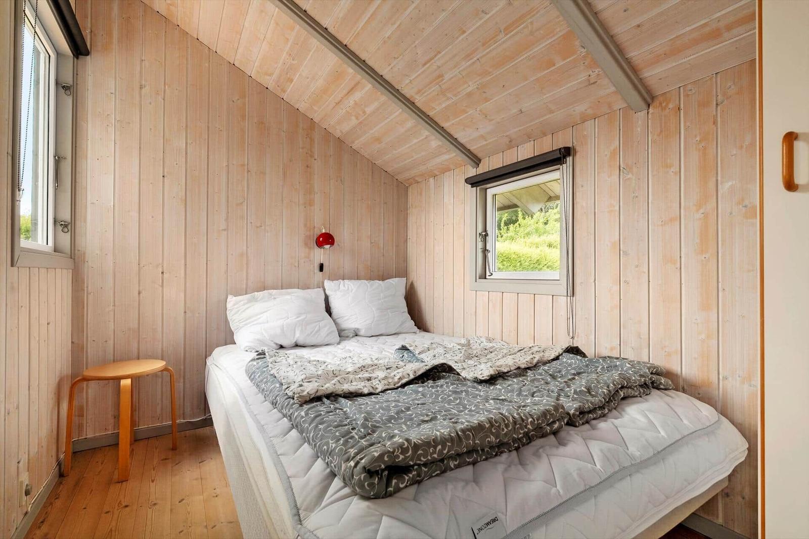 Bedroom with wooden walls, bed, and windows.