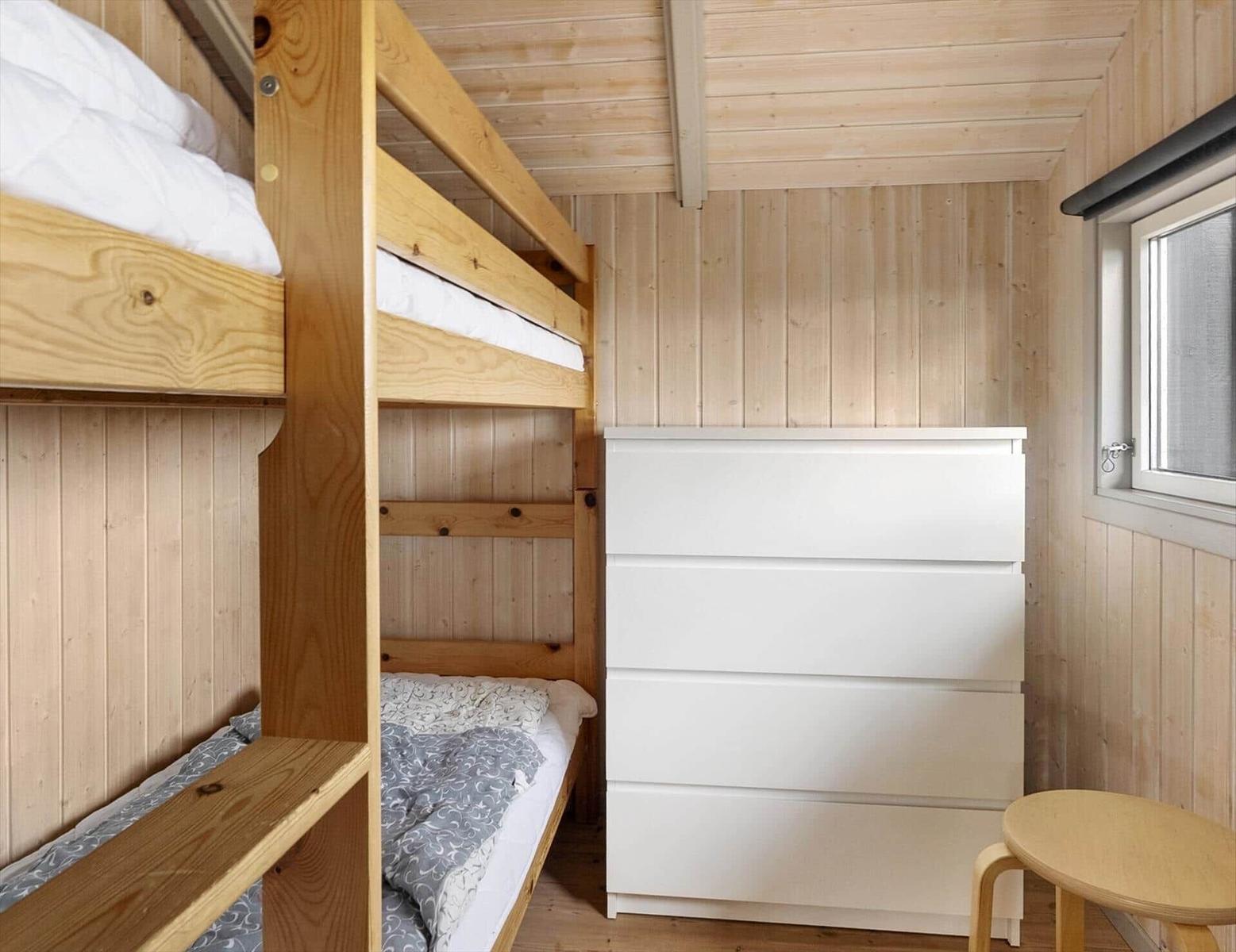 Room with wooden walls, bunk bed, and white drawers.