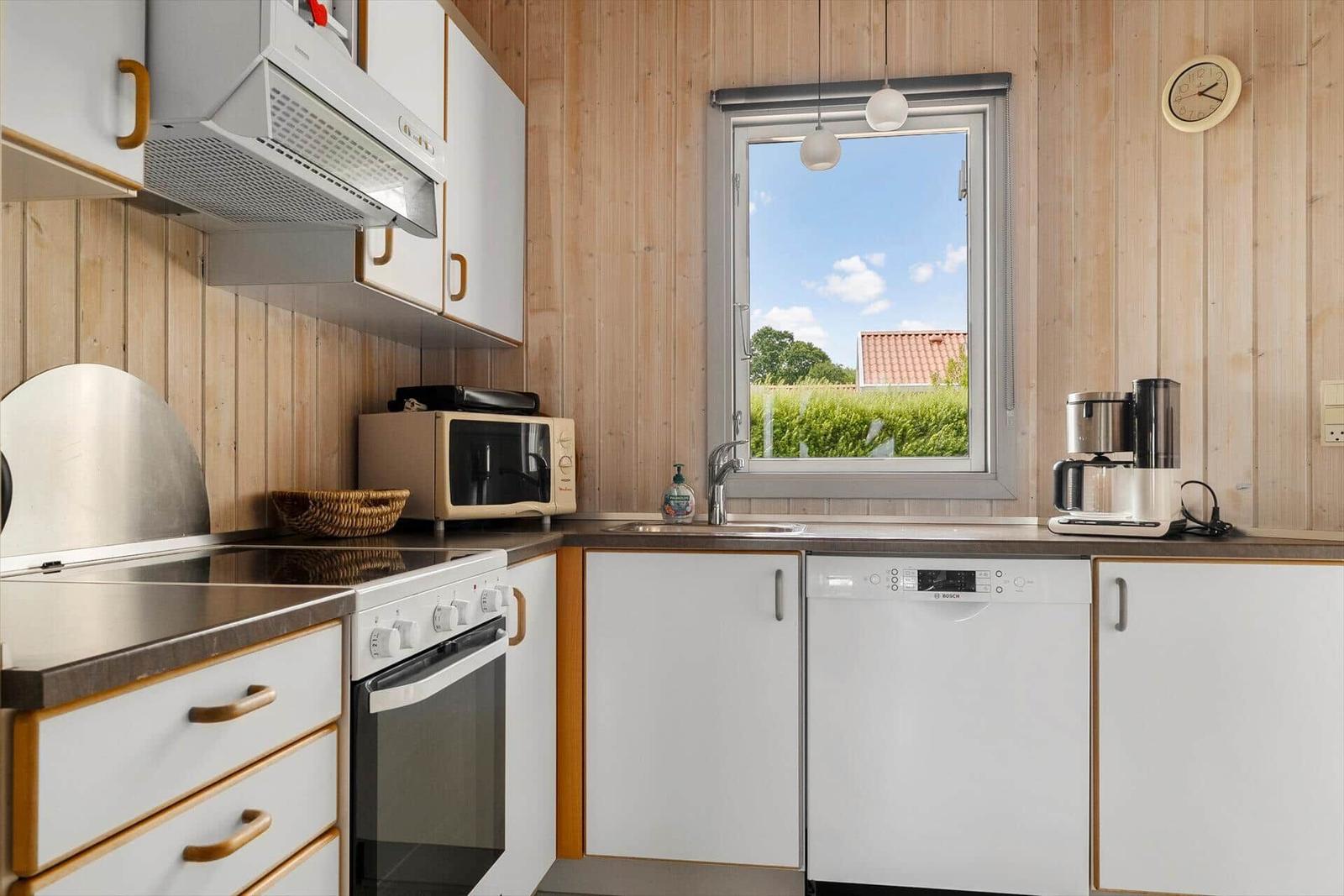 Kitchen with wooden wall, sink, exhaust hood, microwave, and window.