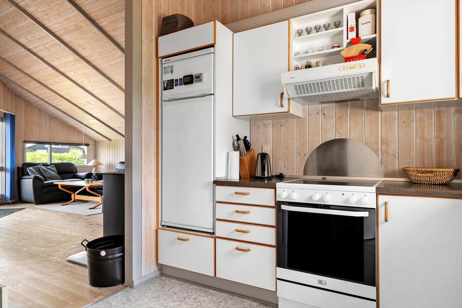 Kitchen with refrigerator, stove, and cabinets. Living room with sofa in background.