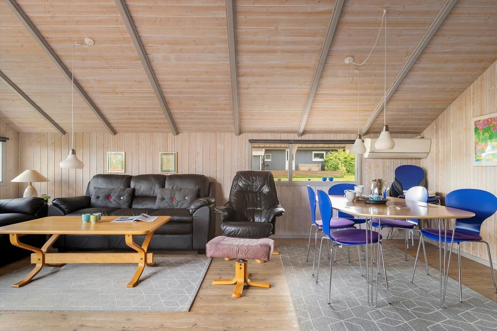 Living and dining area with wooden ceiling, sofa, armchair, and table with chairs.