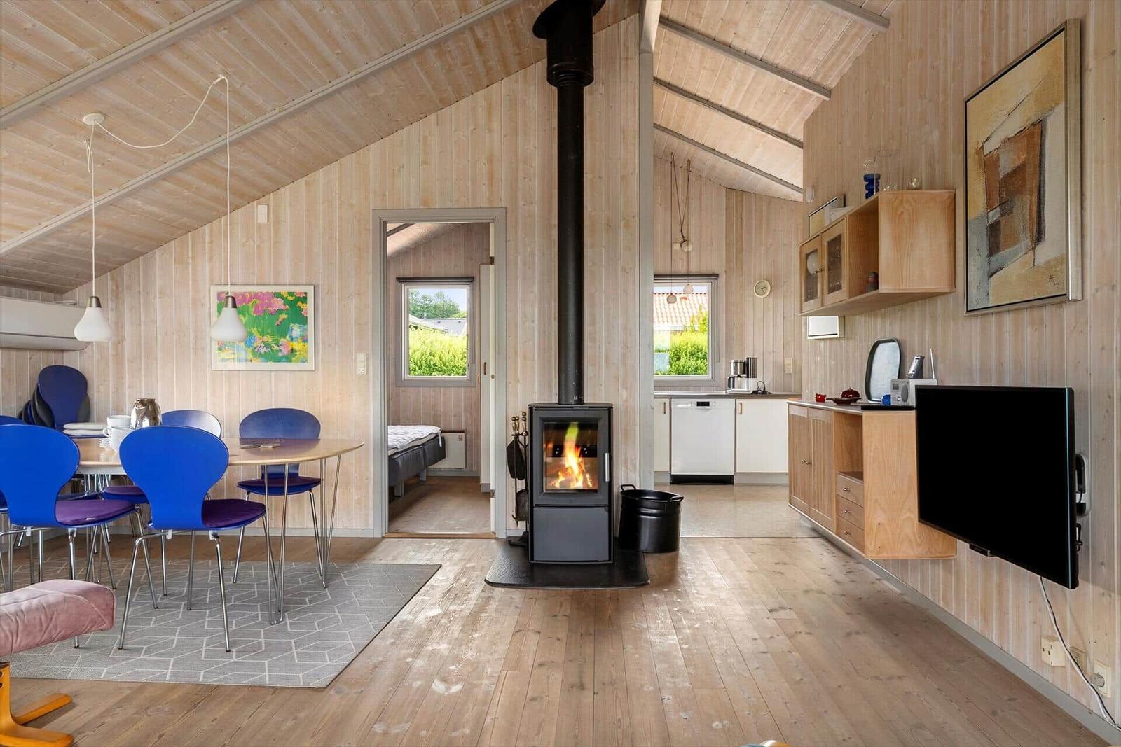 Living space with wood paneling, wood stove, dining table, and kitchen area.