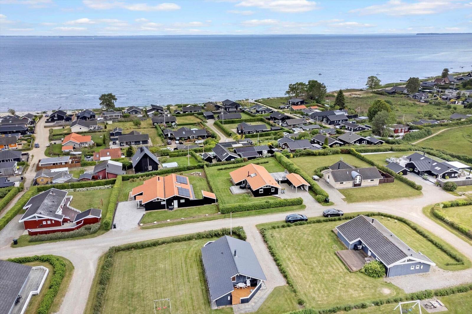 Aerial view of coastal holiday homes with gardens and sea in background.