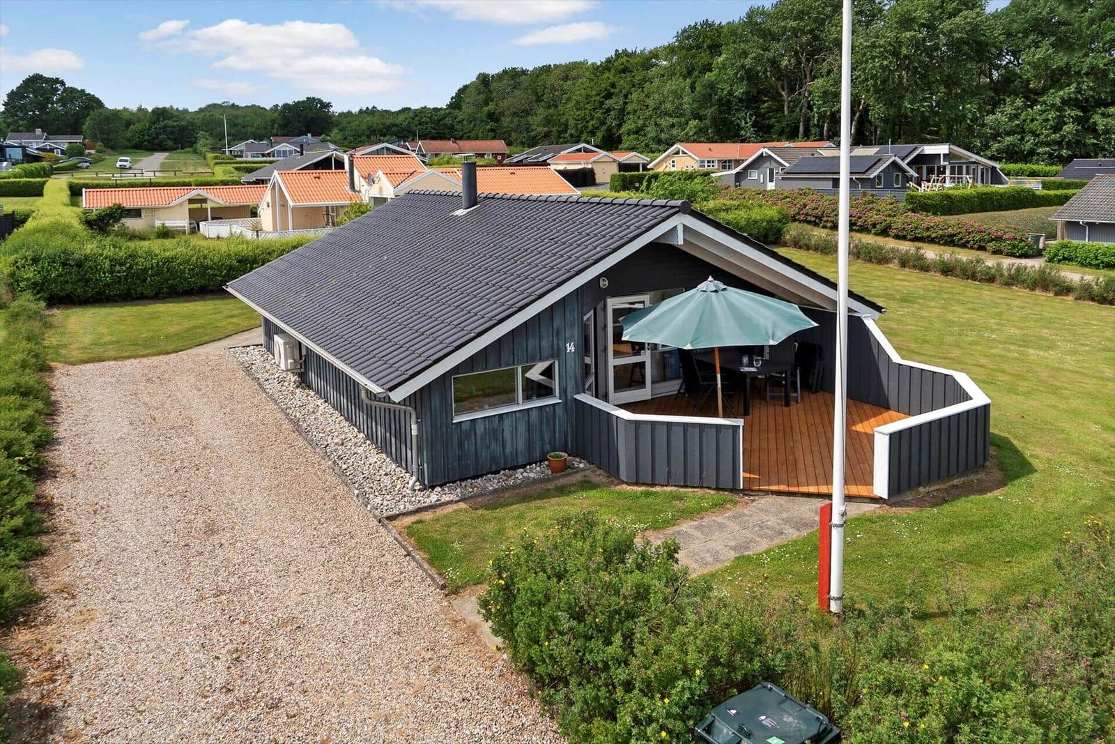 A house with a terrace and umbrella in a green setting.