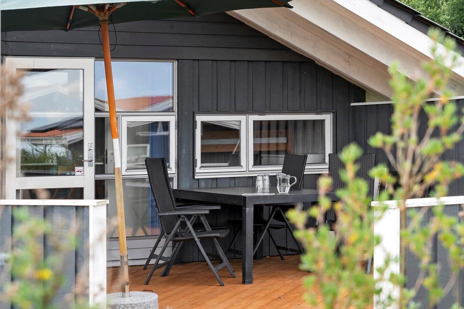 Deck with table, chairs, and umbrella in front of a house with dark wood siding.