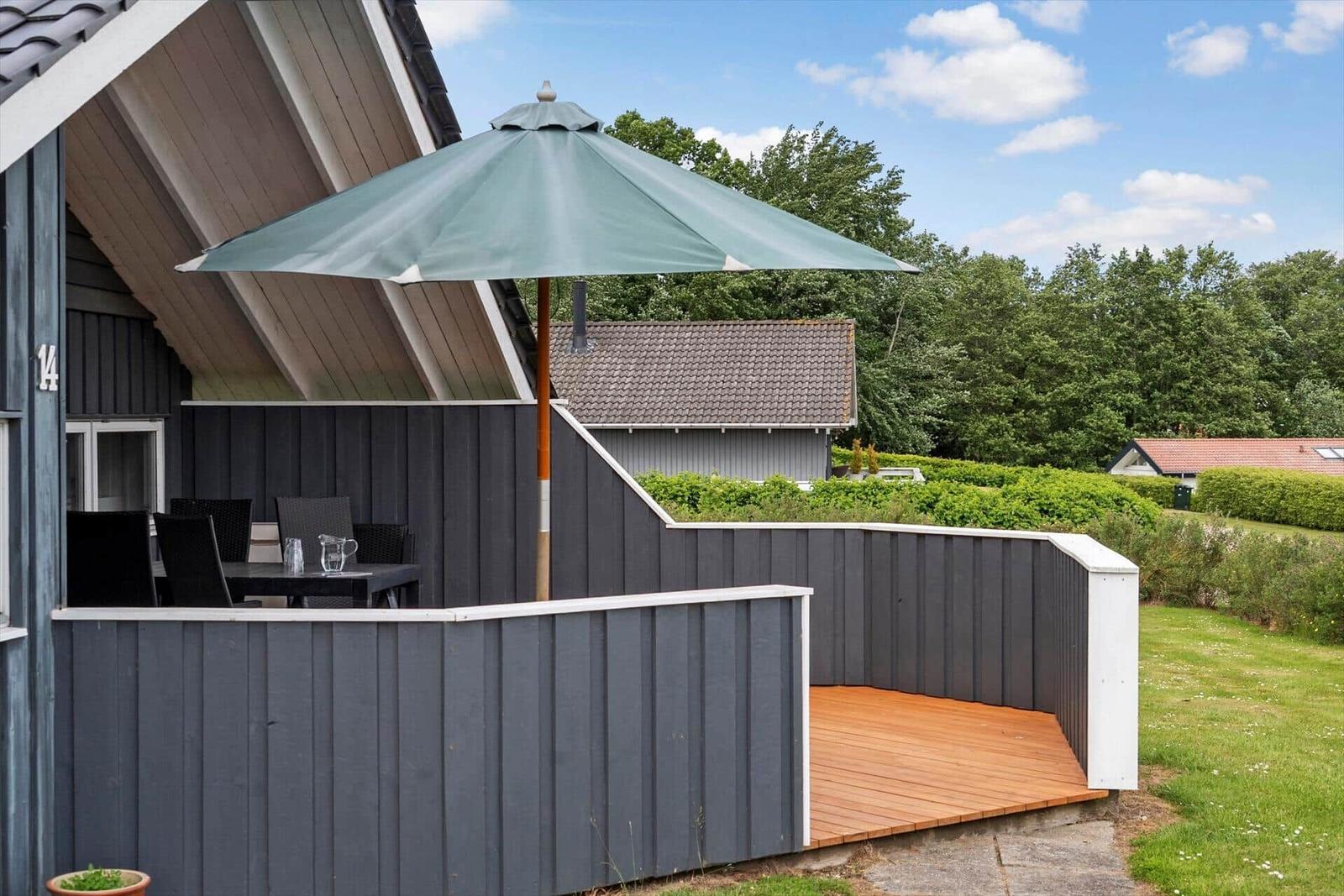 Terrace with umbrella and table. Background: green hedge and sky.
