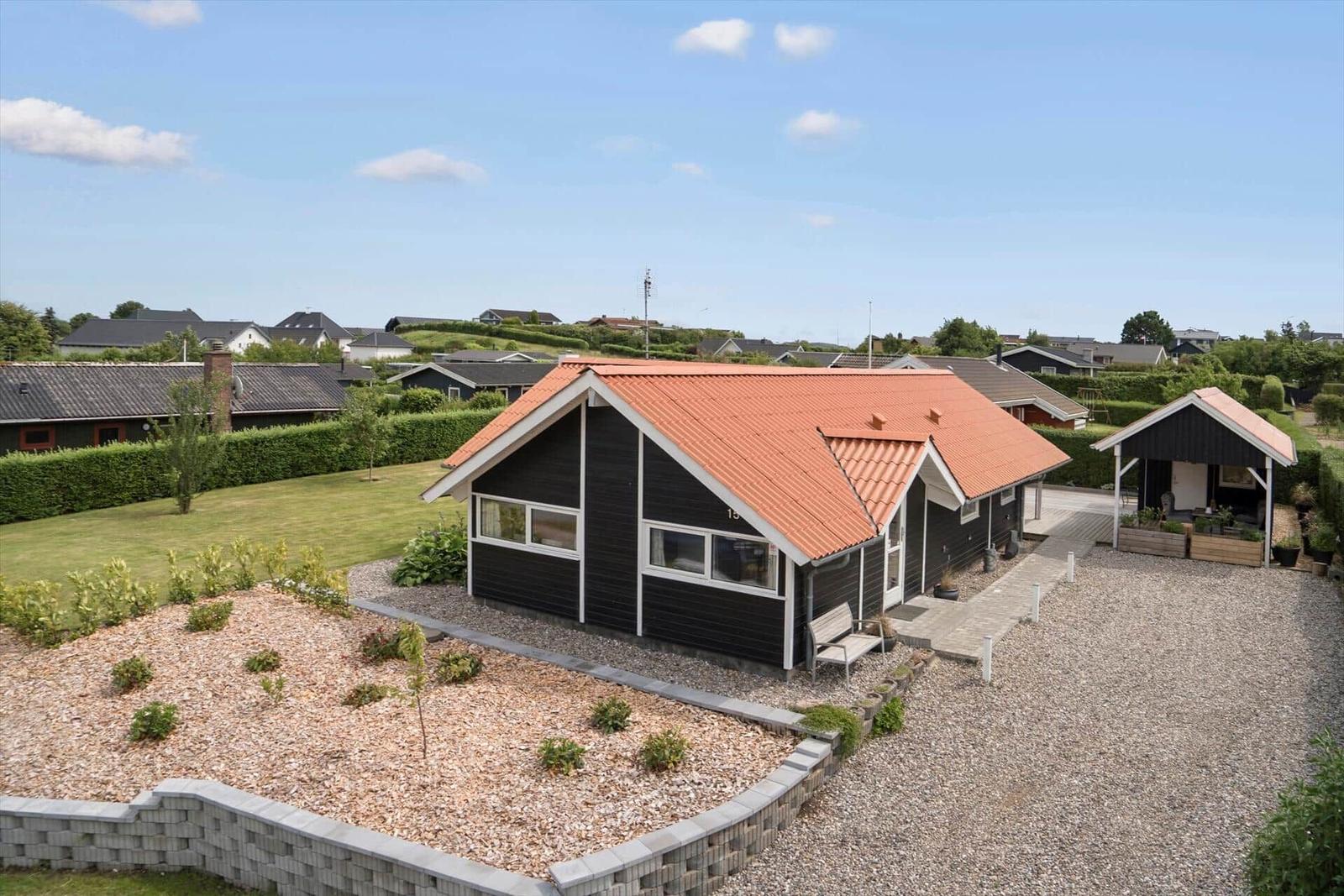 Black wooden house with red roof, landscaped garden and terrace.