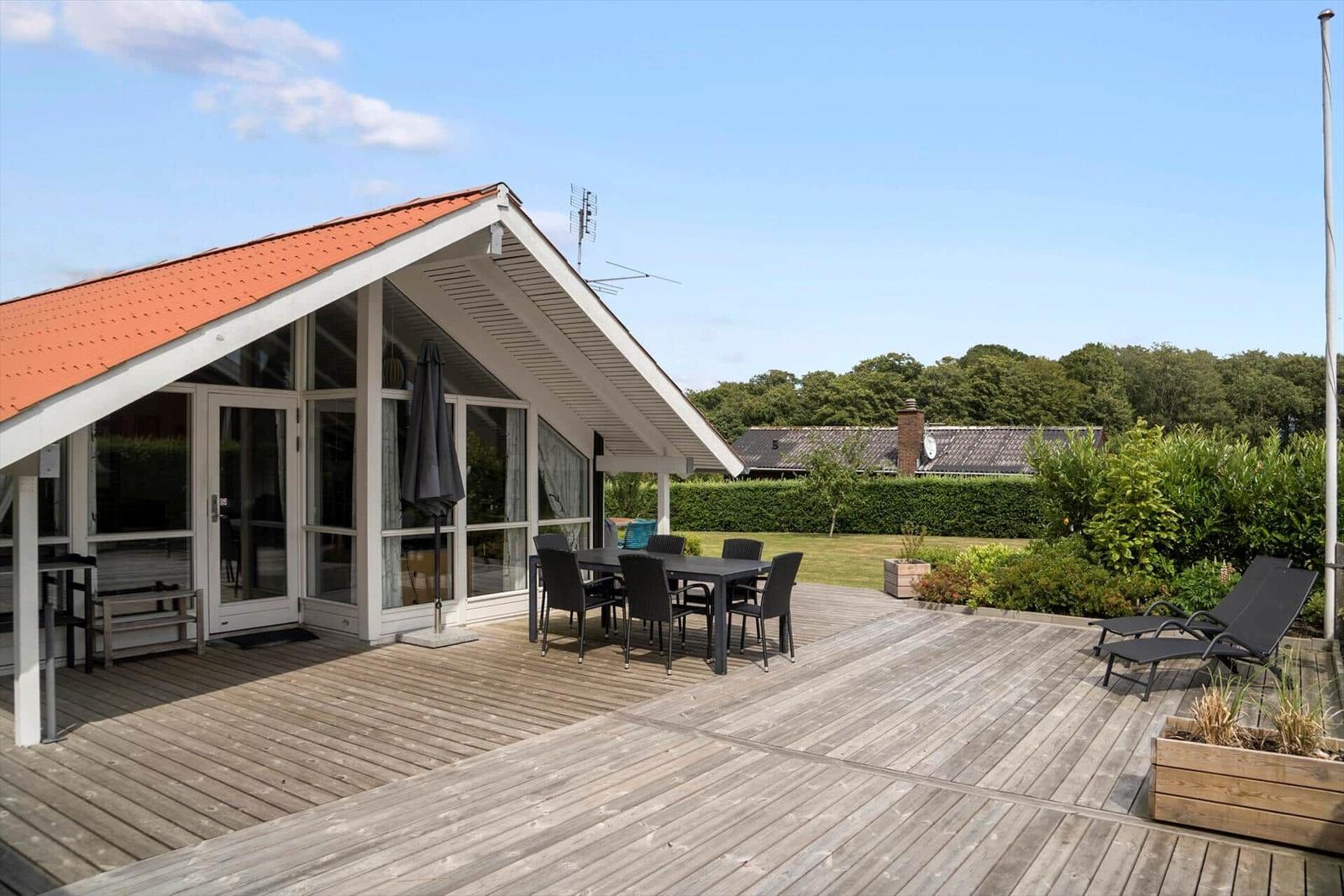 Terrace with table, chairs, and loungers. Backyard with green areas and trees.