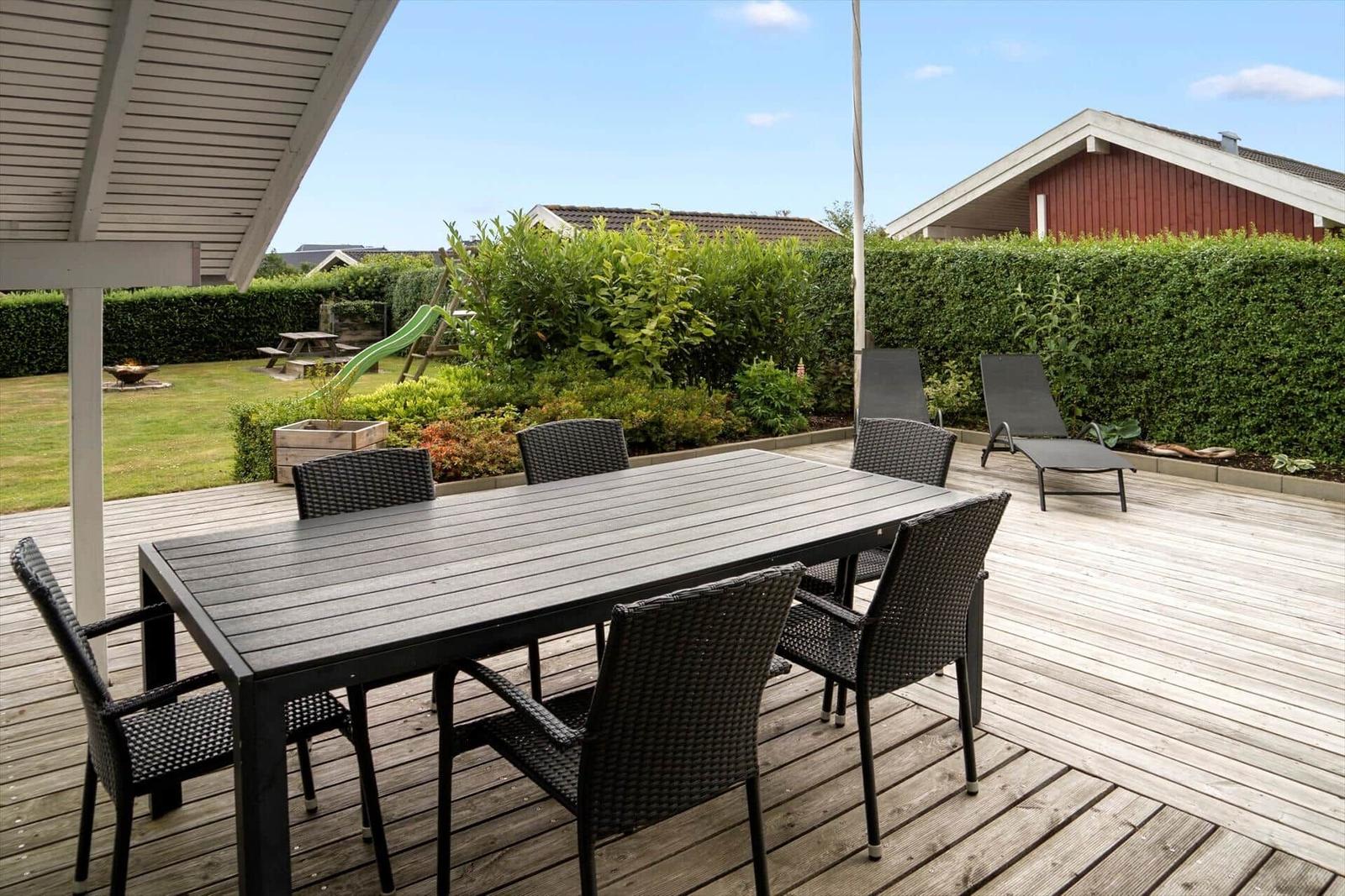 Deck with table and chairs, loungers, and garden with slide.