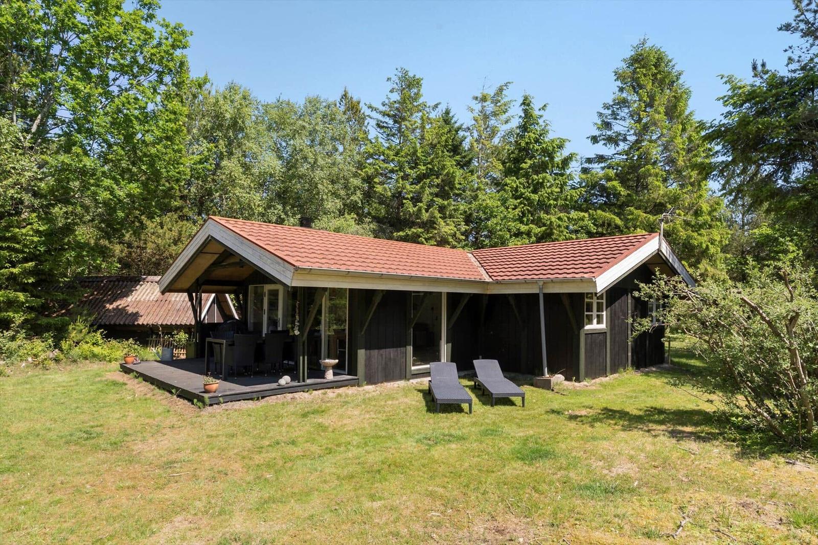 Holzhaus mit Terrasse, Liegestühlen und grünem Garten. Umgeben von Bäumen.