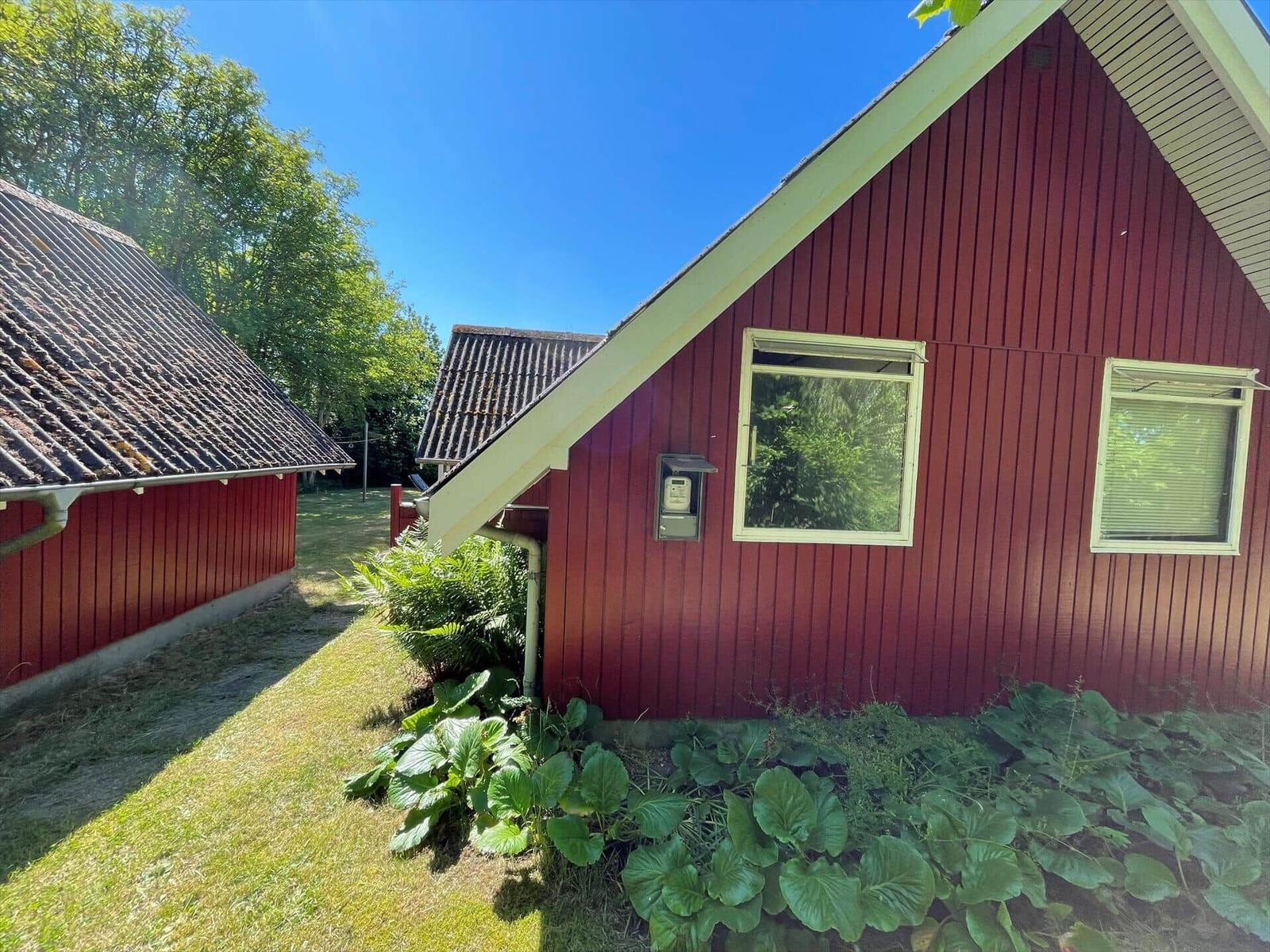 Rotes Holzhaus mit zwei Fenstern und grüner Umgebung.