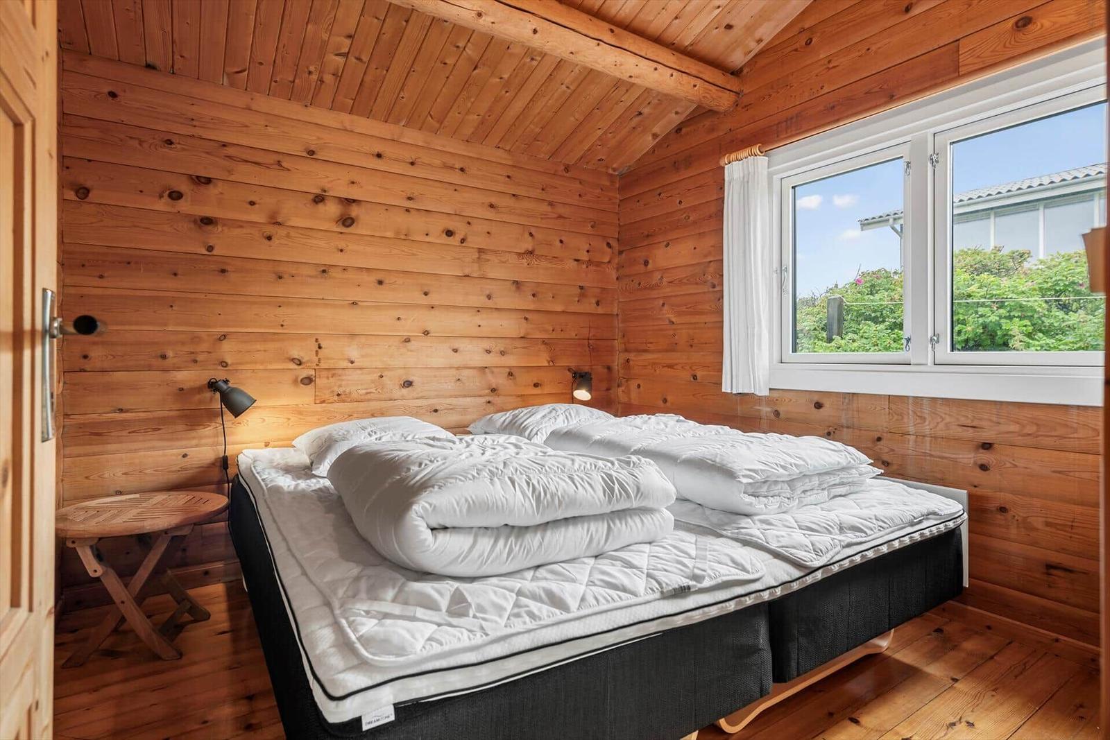 Schlafzimmer mit Holzwand, Bett und Fenster