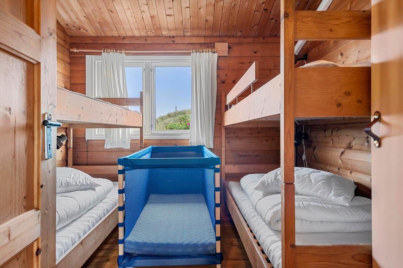 Zimmer mit zwei Stockbetten und einem blauen Kinderbett. Holzwände und Fenster mit Blick nach draußen.