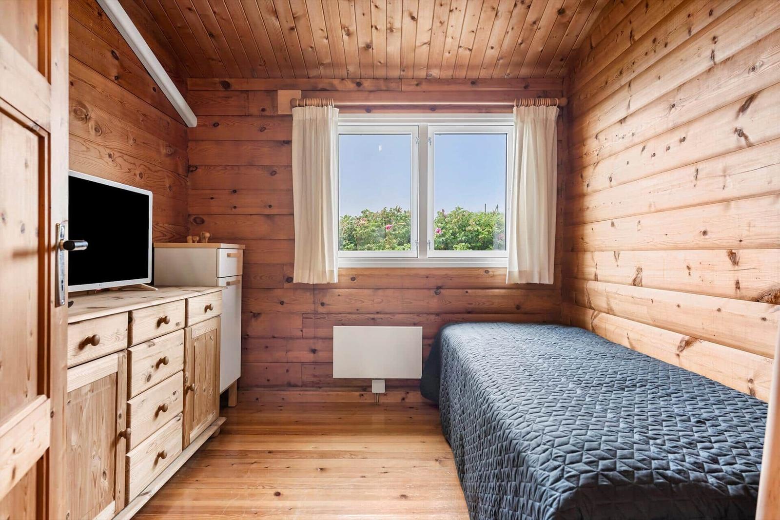 Ein Schlafzimmer mit Holzwänden, Bett, Fenster und TV-Schrank.