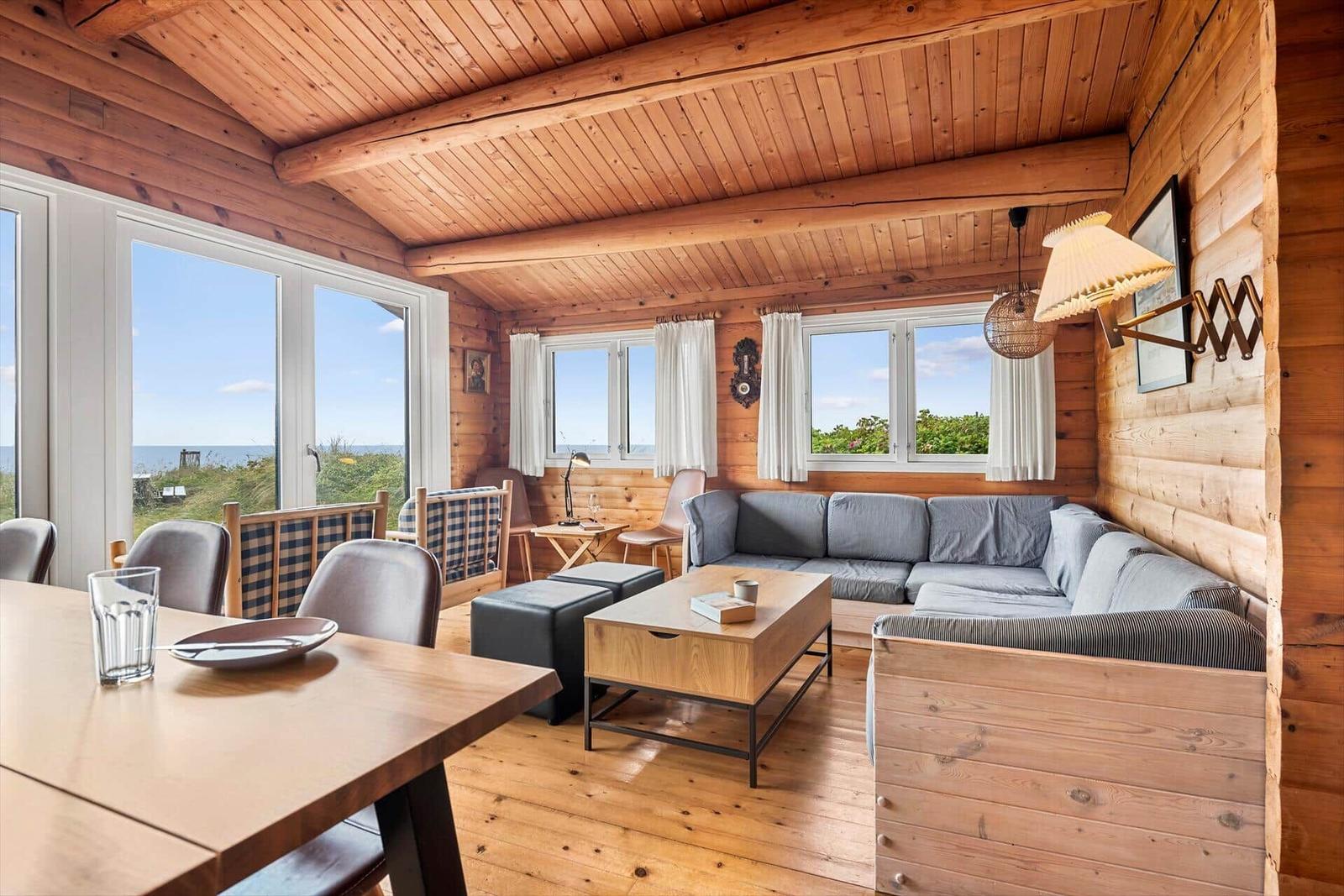Wohn- und Essbereich mit Holzwänden und Meerblick durch große Fenster.