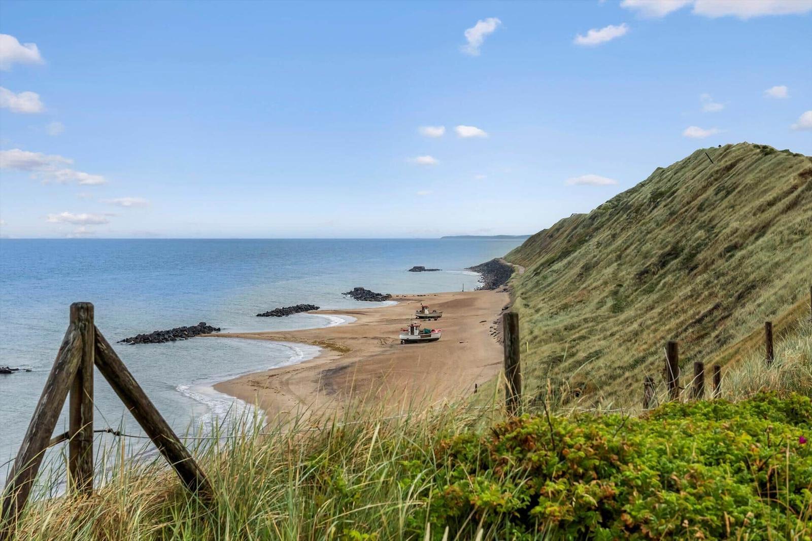 Strand mit Felsen und zwei Booten unter blauem Himmel