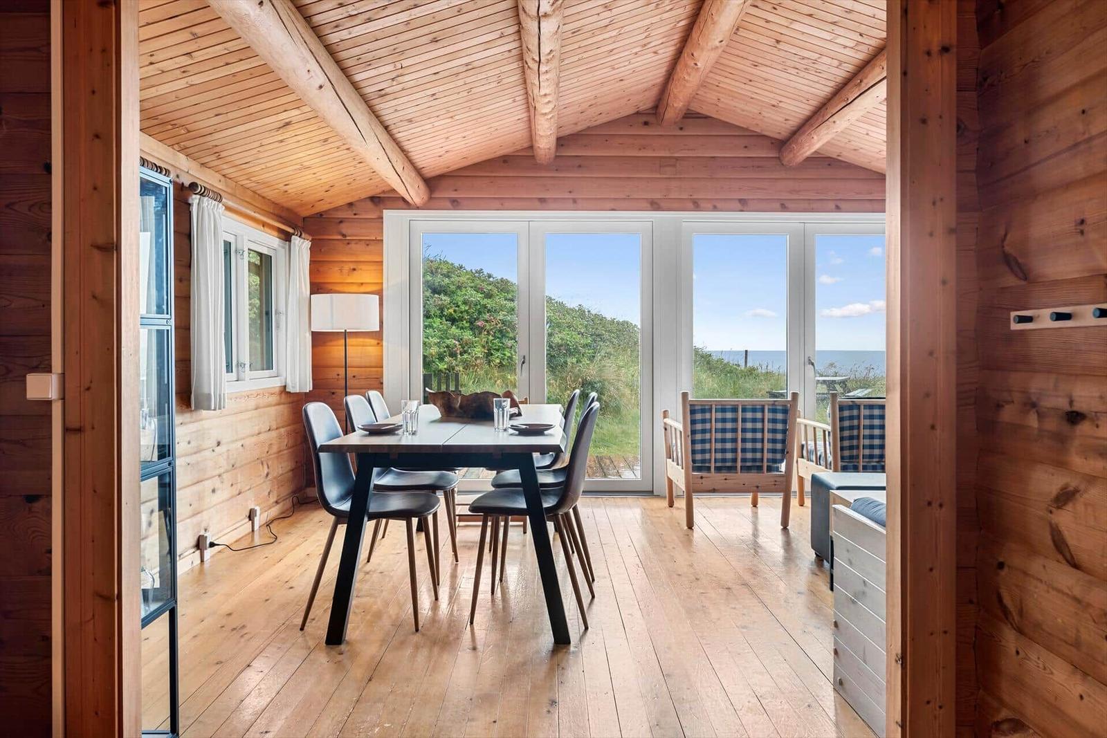 Essbereich mit Tisch und Stühlen, Holzwände und große Fenster mit Meerblick.