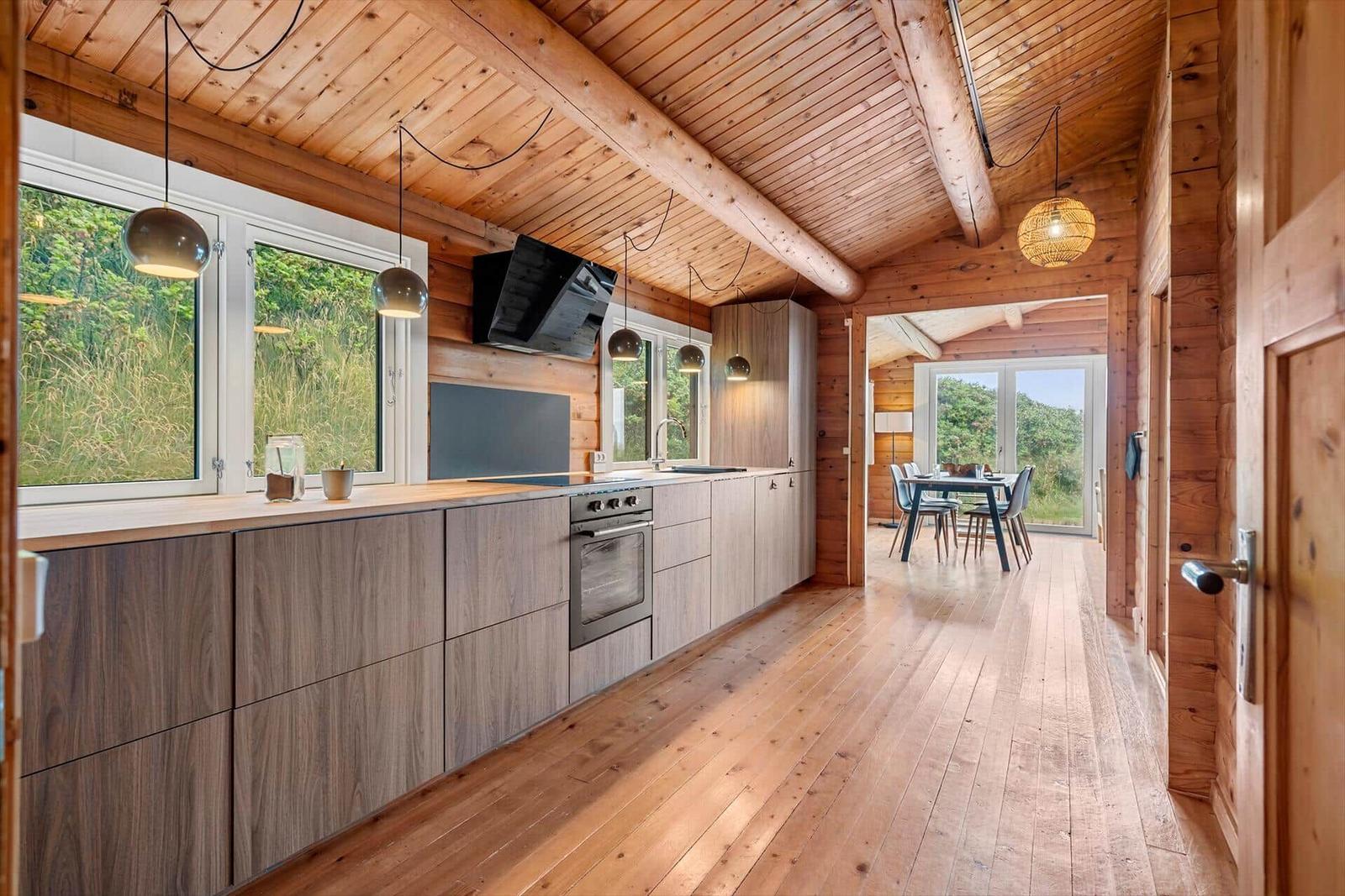 Küche mit Holzboden und -decke, Fenster und Essbereich im Hintergrund.
