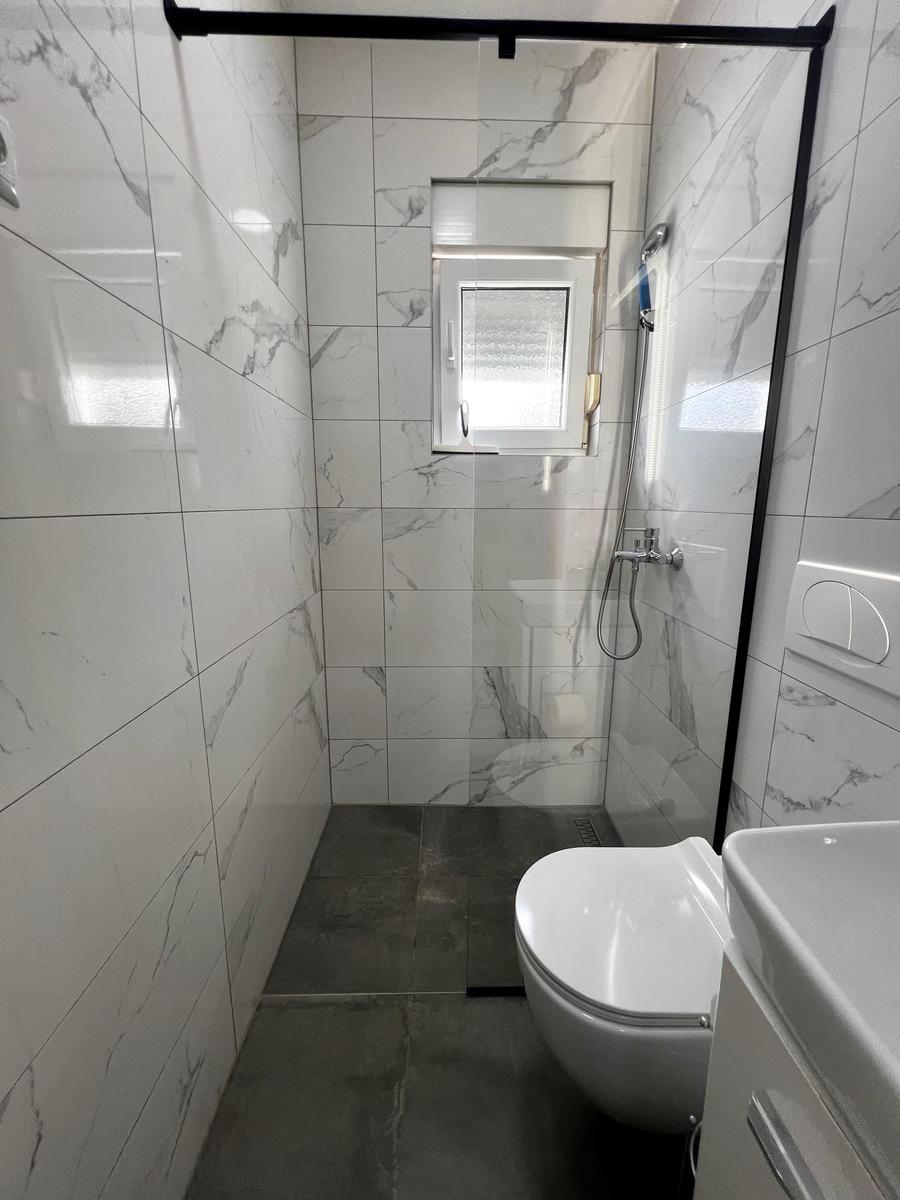 Dusche mit Duschbrause, Toilette und Waschbecken in einem Badezimmer mit Marmorfliesen.