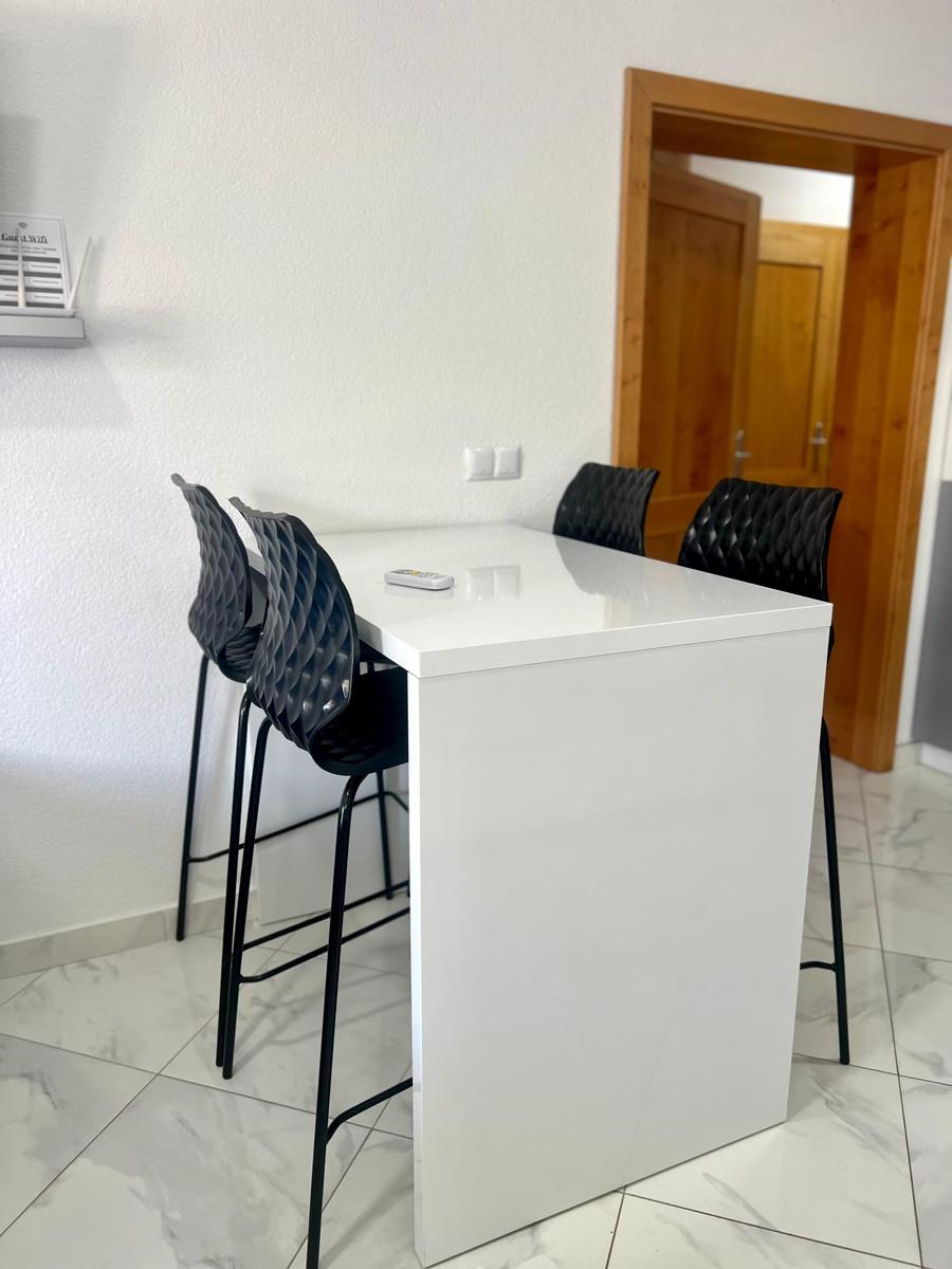 Weißer Esstisch mit schwarzen Barhockern und Marmorfliesenboden.