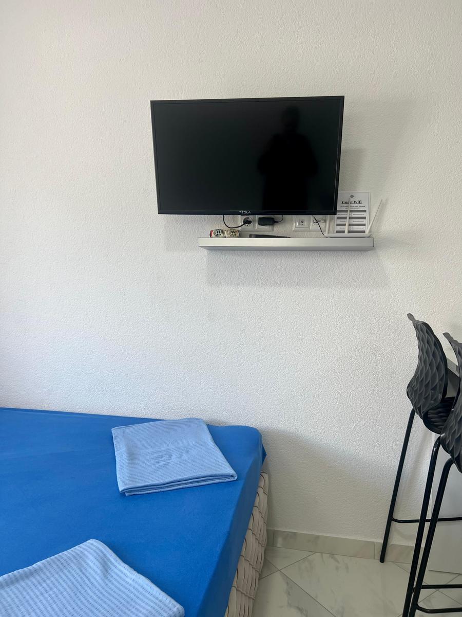 Schlafzimmer mit blauer Matratze, Wand-TV und Stühlen.