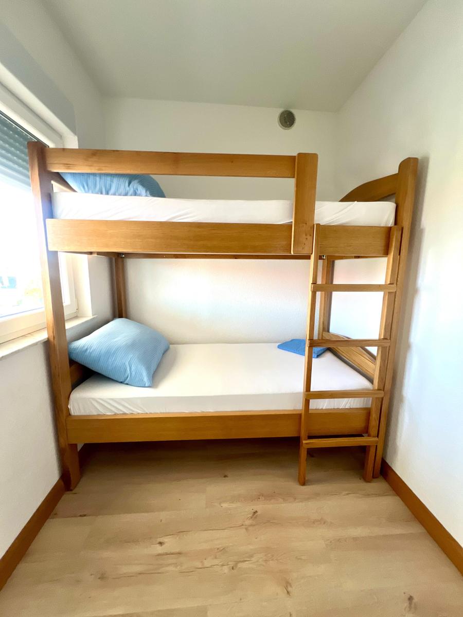 Zimmer mit Holzbett, zwei Matratzen und blauen Kissen.