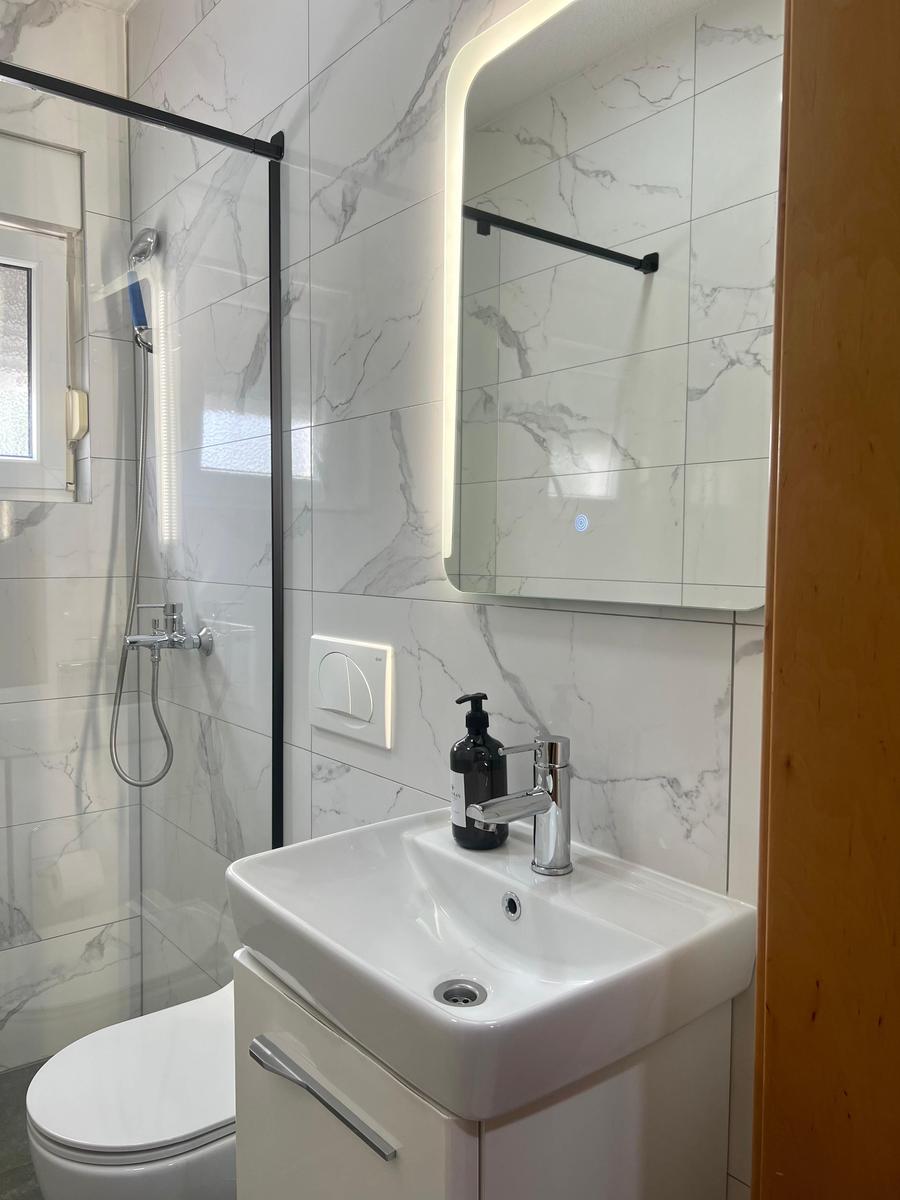 Badezimmer mit Dusche, Waschbecken und beleuchtetem Spiegel