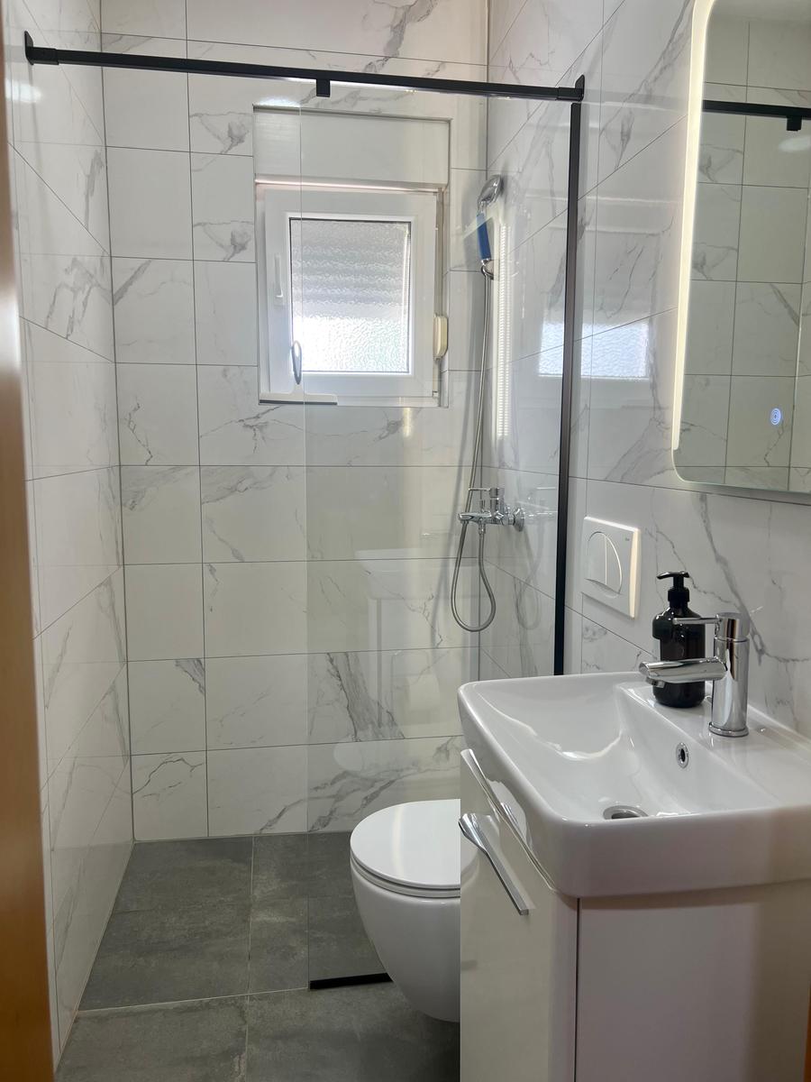 Badezimmer mit Dusche, Waschbecken und Toilette. Weiße Fliesen und Spiegel.