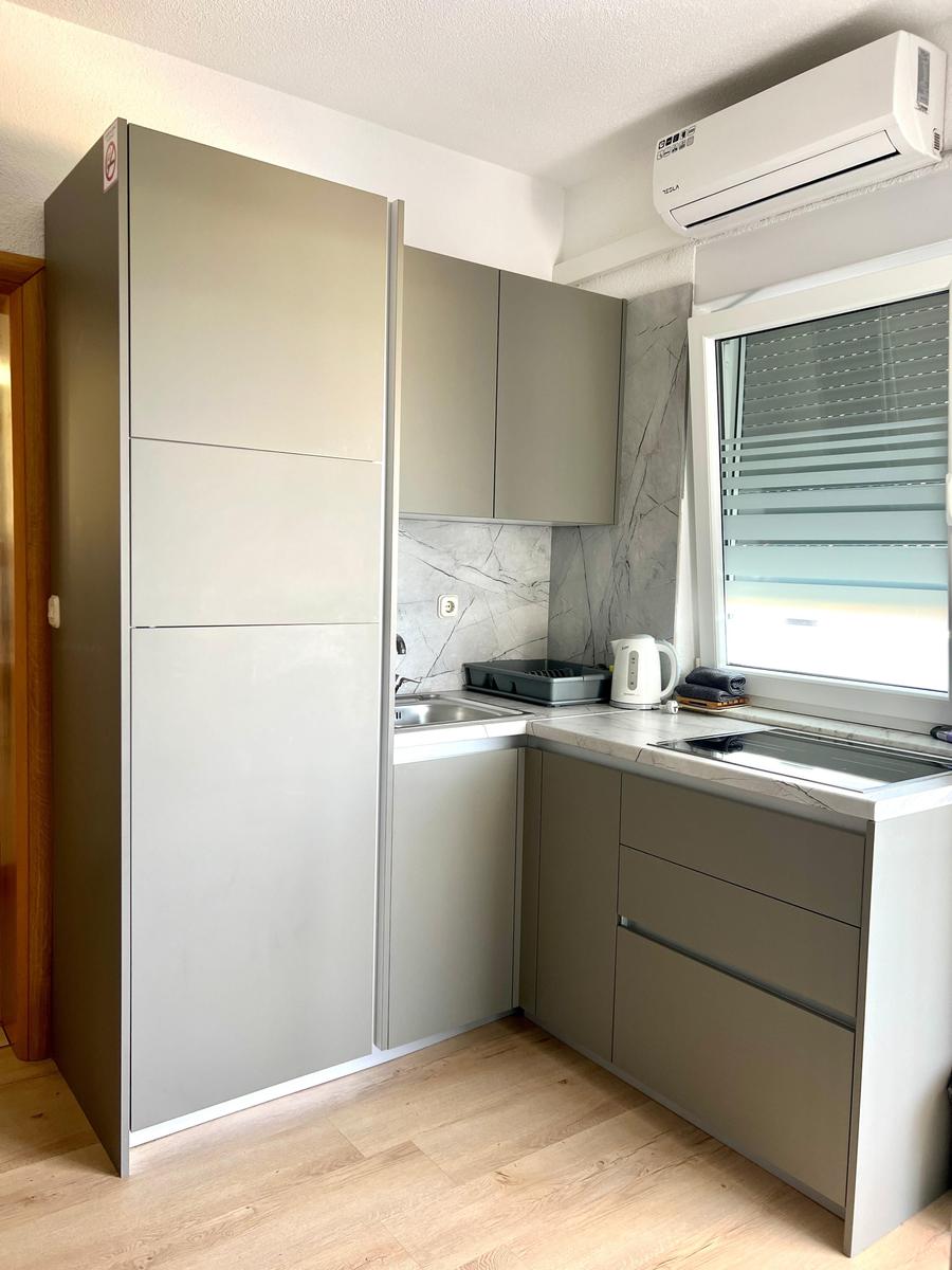 Küche mit grauen Schränken, Arbeitsplatte und Fenster mit Jalousie.