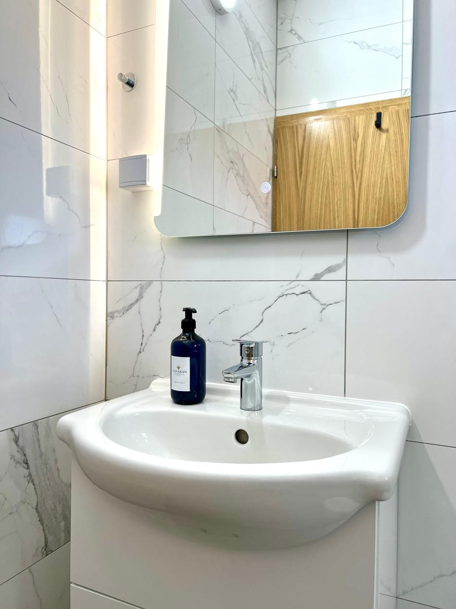 Waschbecken mit Spiegel und Seifenspender an marbliertem Wandverkleidung.