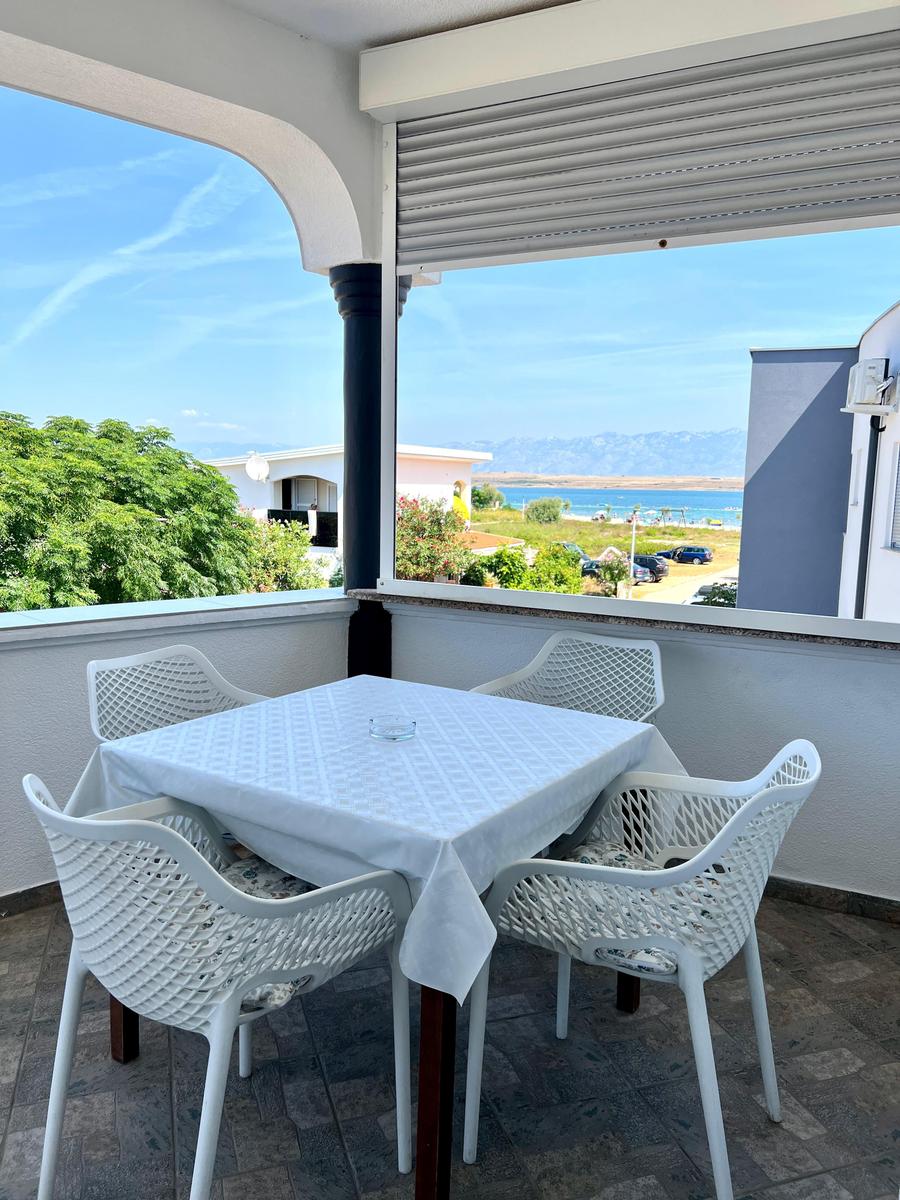 Terrasse mit weißem Tisch und Stühlen, Blick auf See und Berge.
