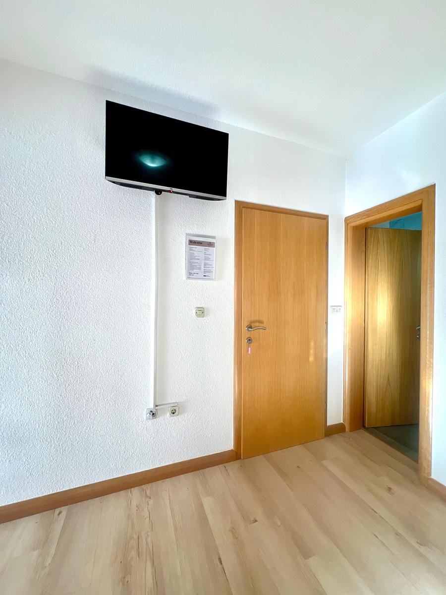 Wohnraum mit Wandfernseher, Holztür und angrenzender Tür.