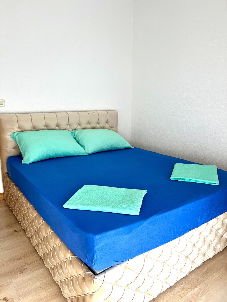 Schlafzimmer mit Bett, blauer Bettwäsche und hellgrünen Kissen.