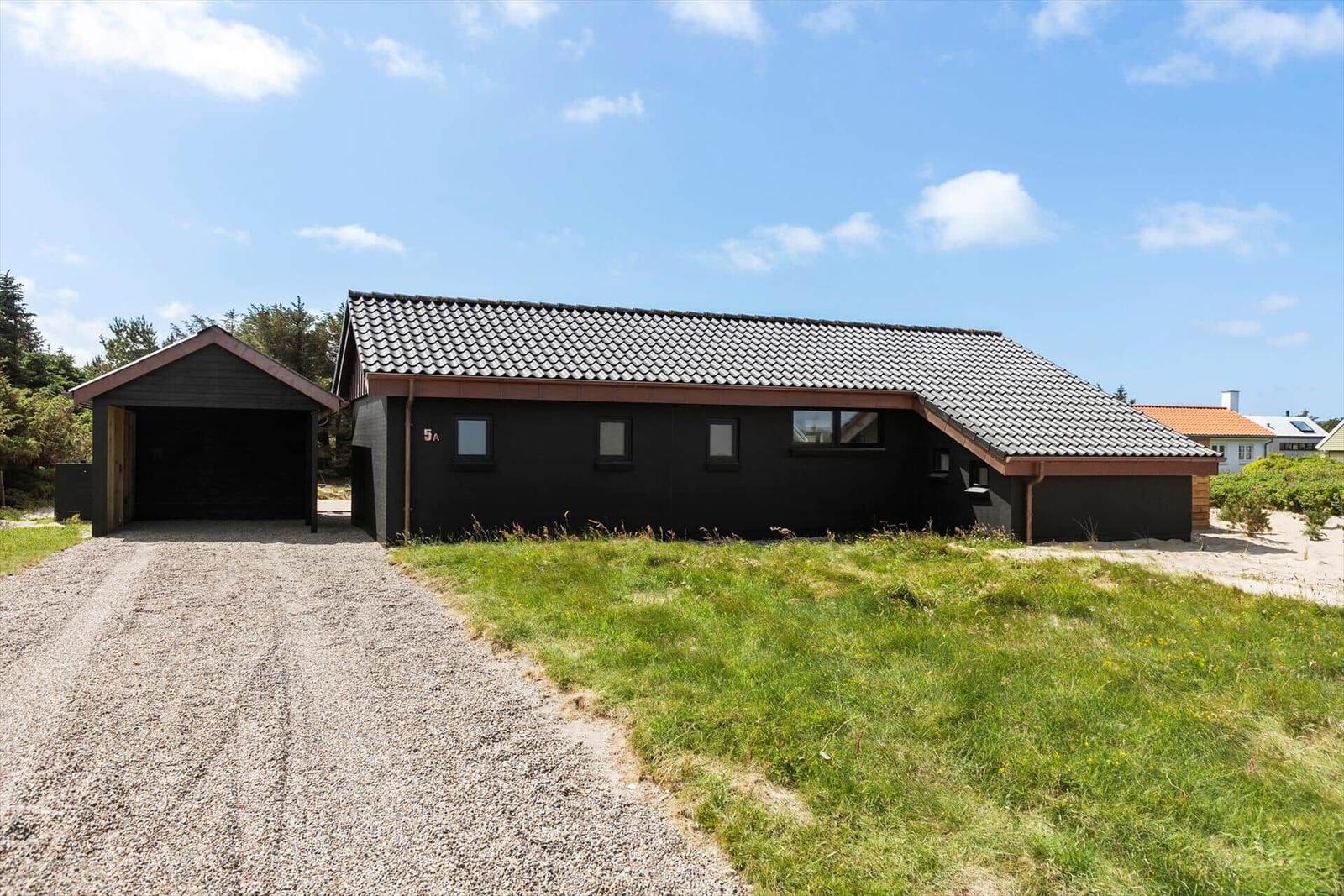 Schwarzes Haus mit Garage und grünem Grundstück unter blauem Himmel.