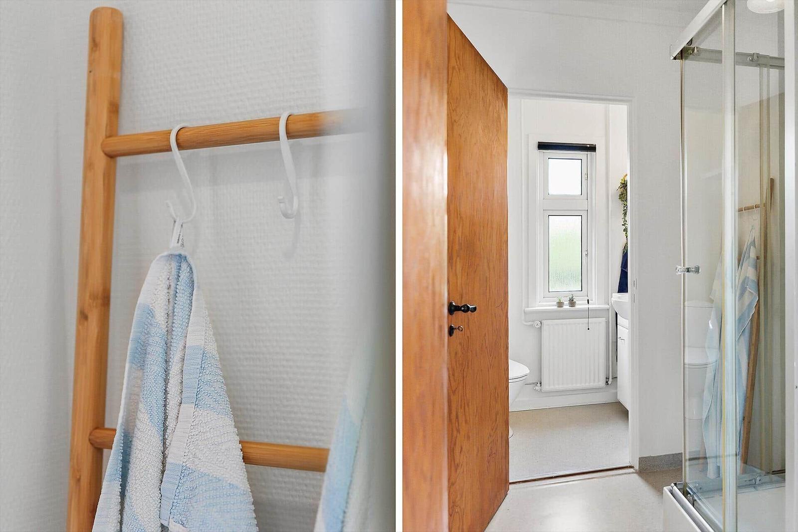 Bathroom with shower, toilet, and window. Wooden towel rack with towel.