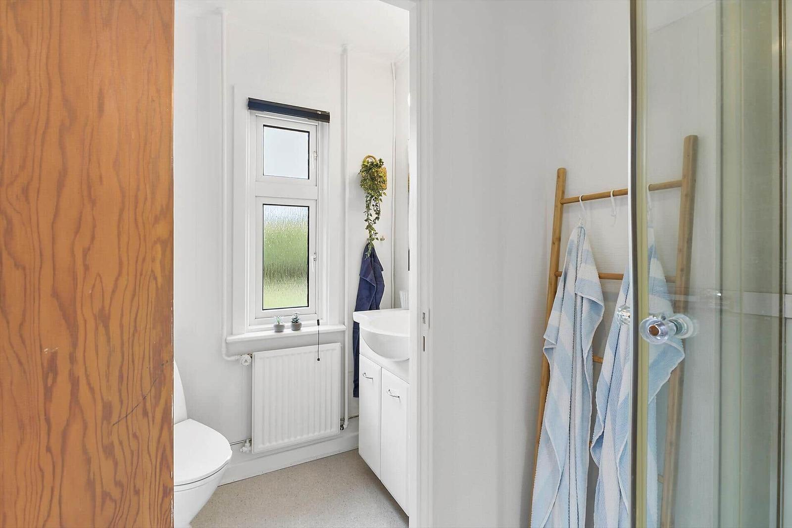 Bathroom with shower, sink and toilet. Window with plants and towel rack.