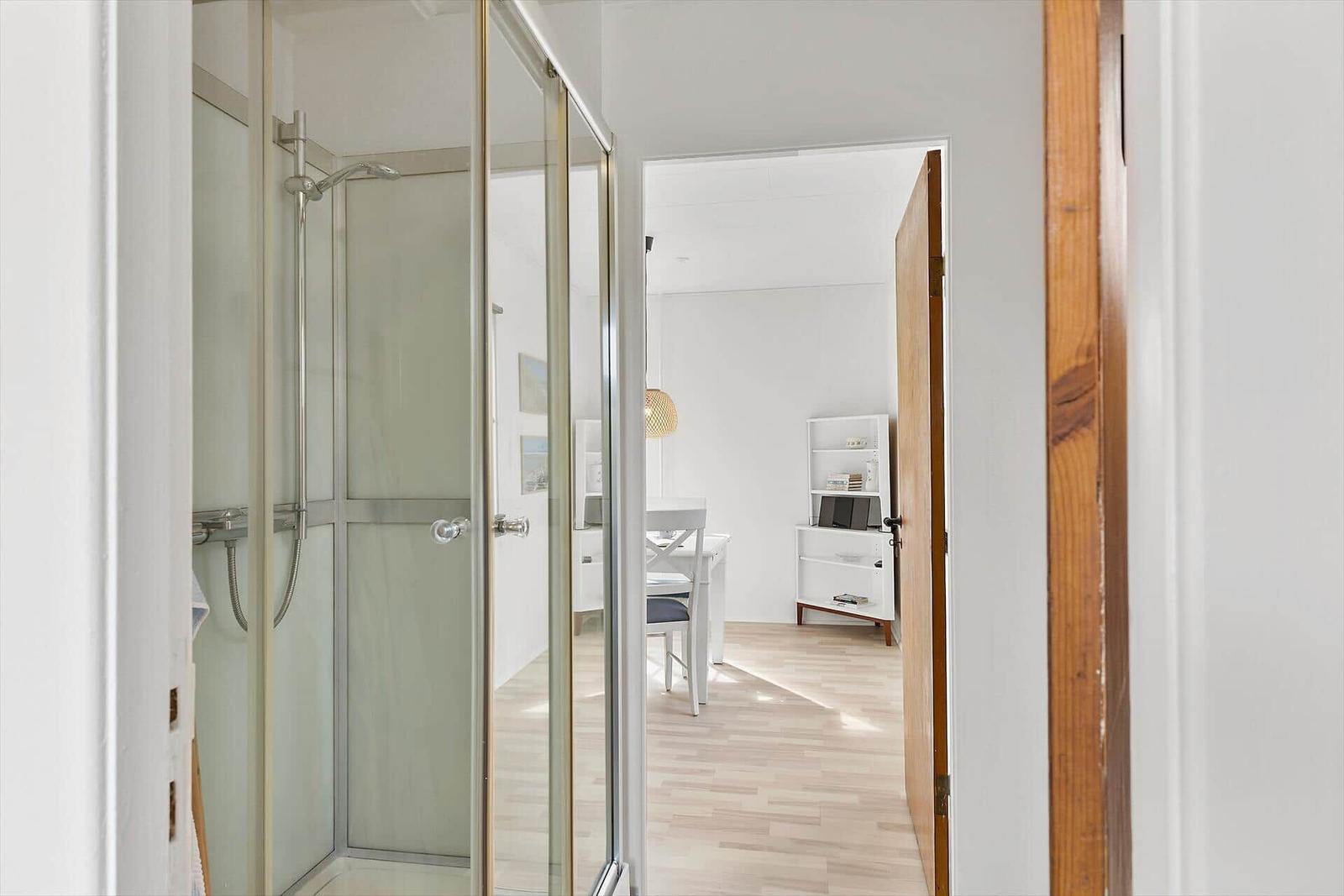 Shower area with glass enclosure. View into living area with table and chair.