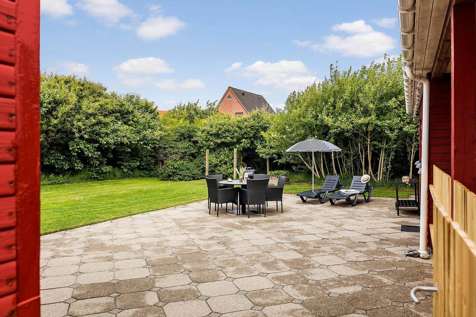 Terrace with table, chairs, and loungers under umbrella.