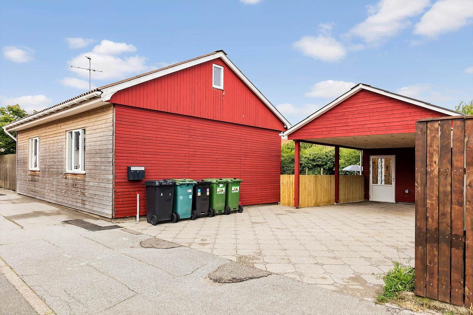 Red house with carport and trash bins in front