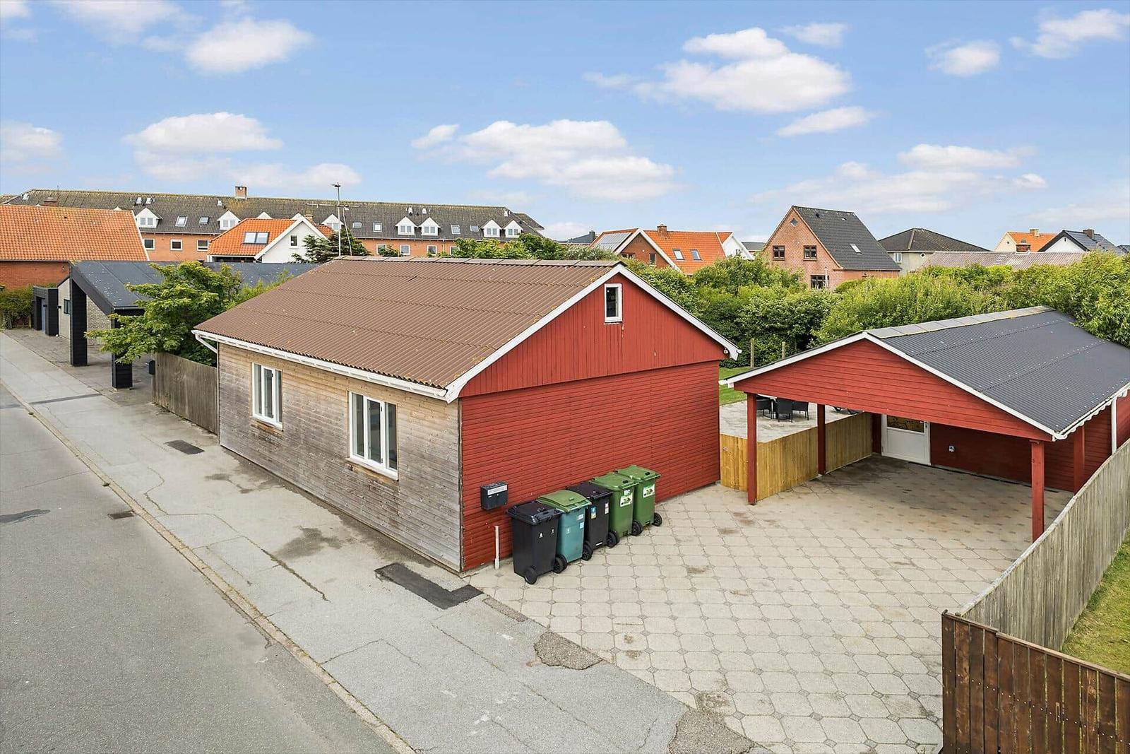 Red house with garage and paved yard. Several trash bins are in front of the building.