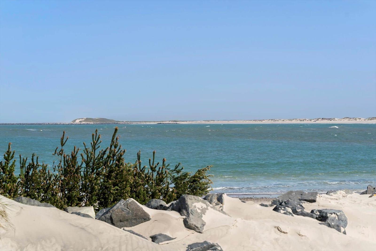 Beach with sand dunes and rocks, view of the sea and an island in the background.