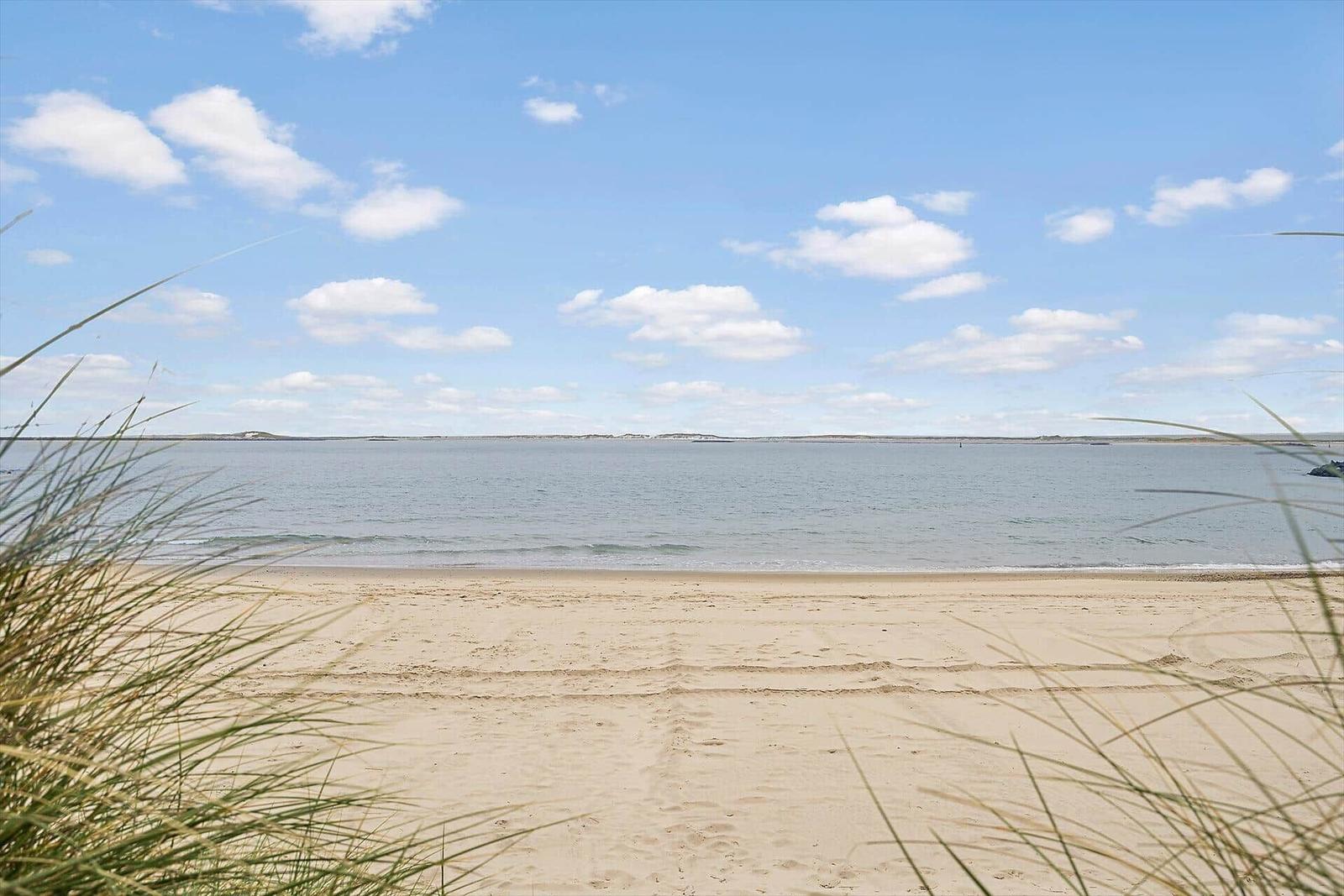 Beach with sand and water under blue sky with white clouds.