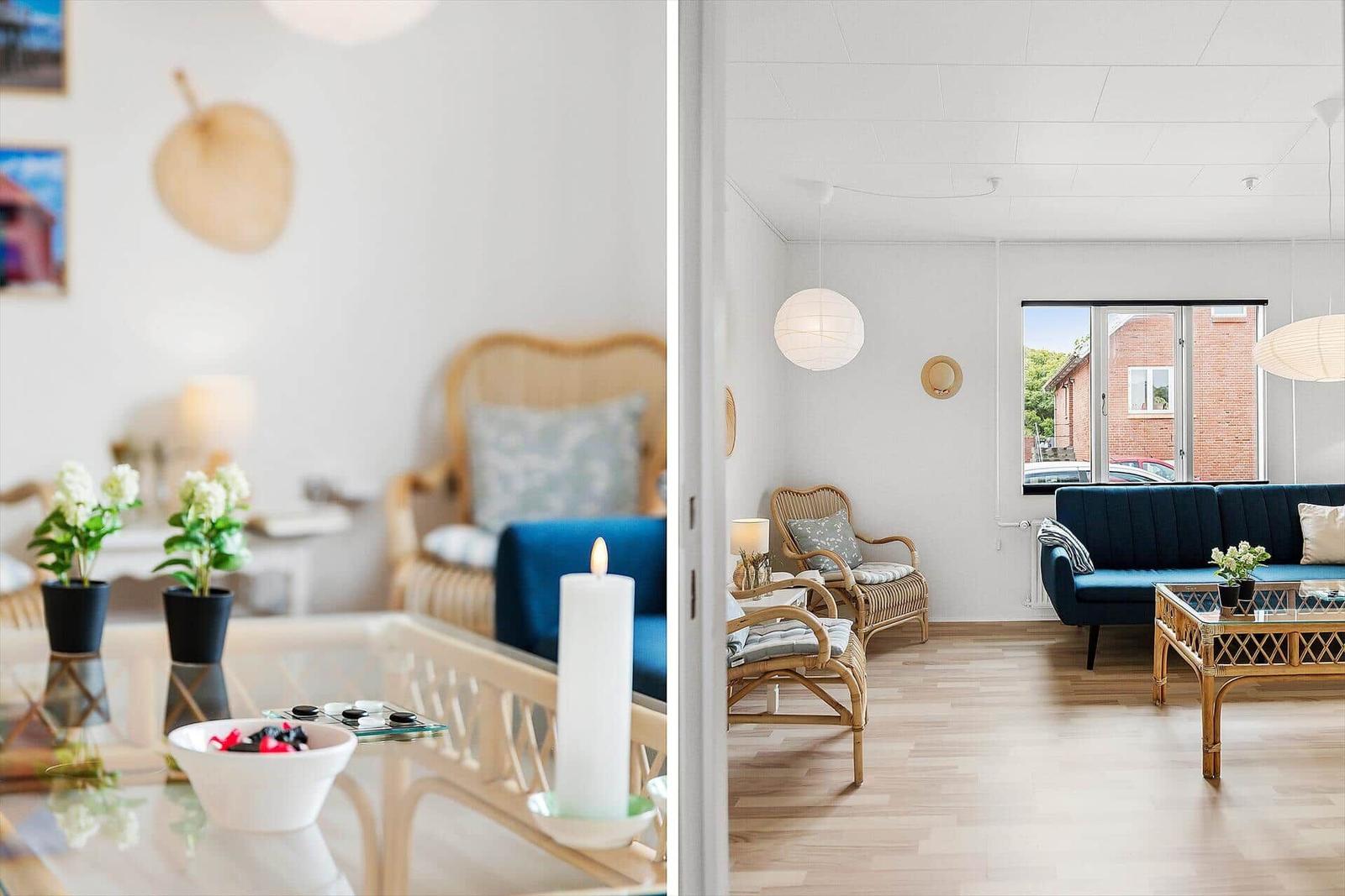 Living room with blue sofa, rattan furniture, and glass table. View of street through window.